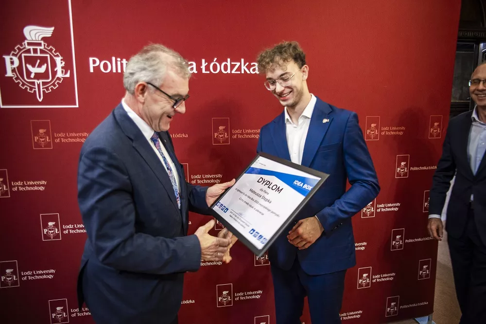 Dwóch uśmiechniętych mężczyzn, jeden z nich wręcza drugiemu dyplom.