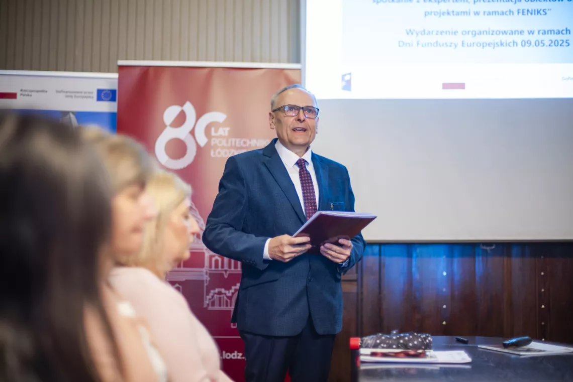 Mężczyzna przemawia na spotkaniu, z tyłu widoczny ekran i banery