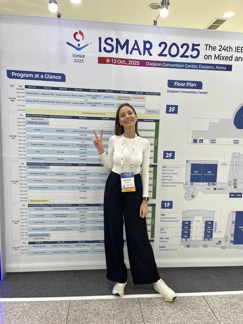 Uśmiechnięta doktorantka na tle ścianki międzynarodowego sympozjum ISMAR