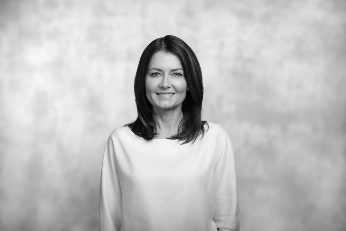 Usmiechnięta kobieta z ciemnymi włosami rozpuszczonymi na ramiona, w białej bluzce