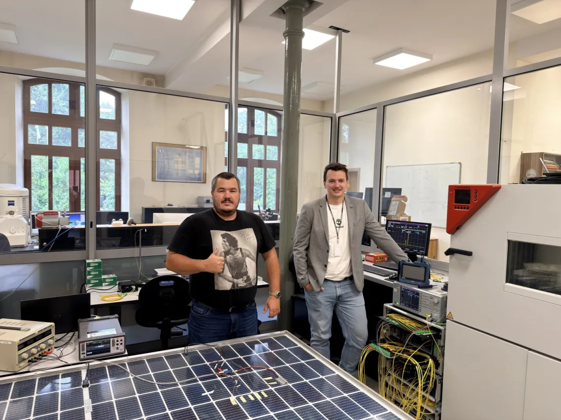 Dwóch młodych mężczyzn  w laboratorium wyposażonym w nowoczesny sprzęt, na pierwszym planie panel fotowoltaiczny