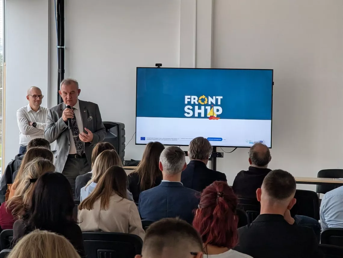 Mężczyzna z mikrofonem przemawia do osób zebranych w sali seminaryjnej