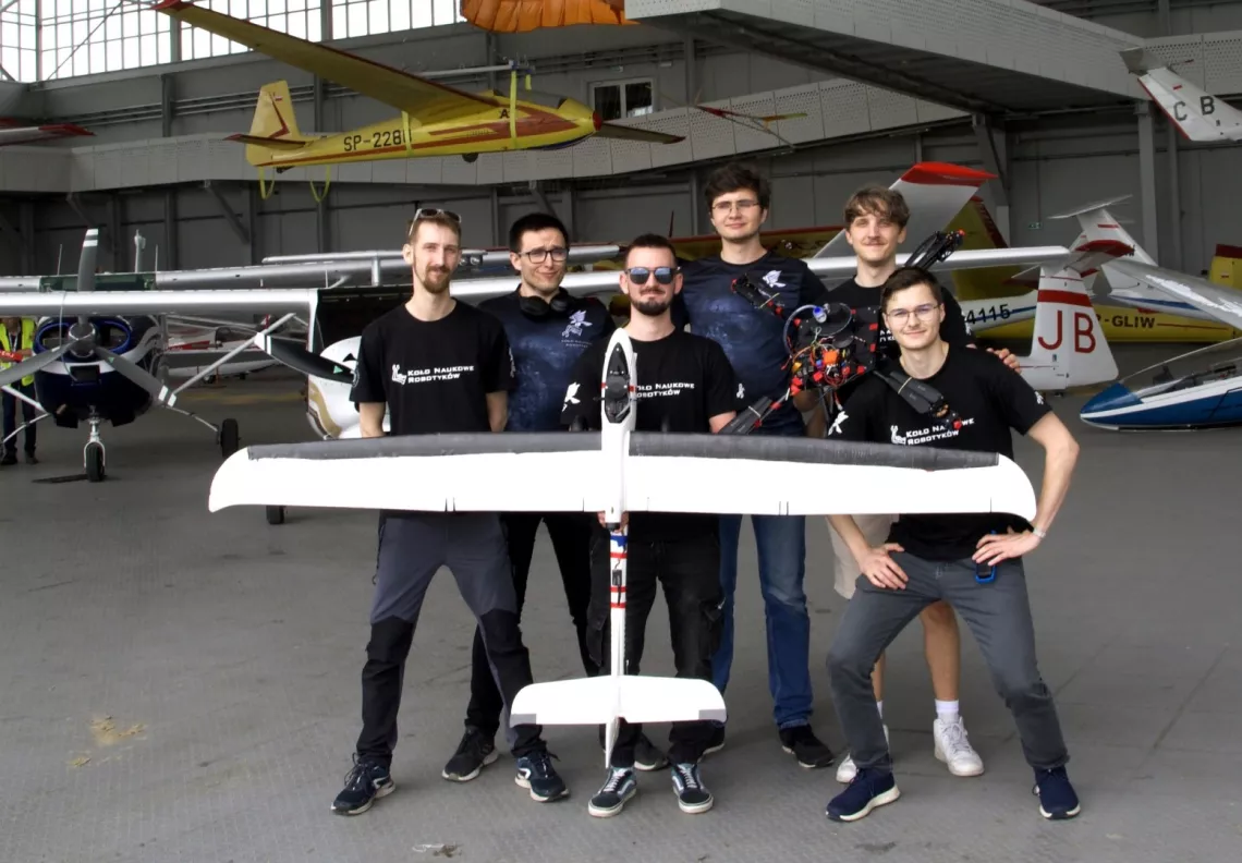 Grupa studentów stoi w hangarze, trzymają w rękach dron z oprzyrządowaniem