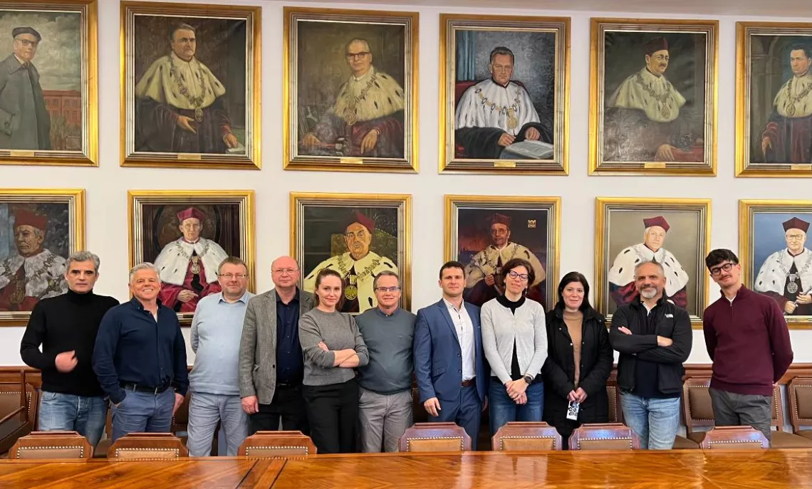 Grupa osób stojąca przed ścianą z portretami rektorów.