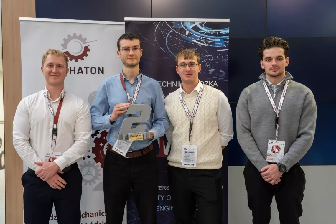 Czterech studentów pozuje do zdjęcia, jeden z nich trzyma w reku cyfrę 2