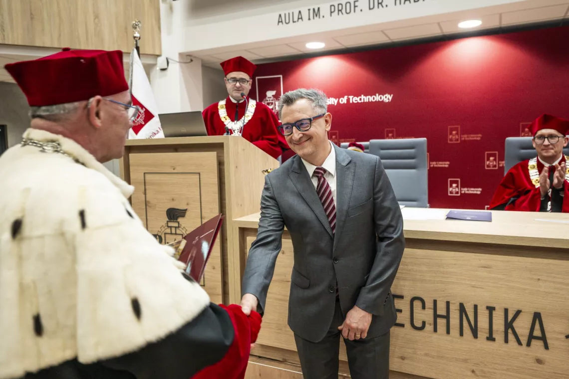 Mężczyzna w eleganckim garniturze odbiera gratulacje od rektora ubranego w ceremonialny strój