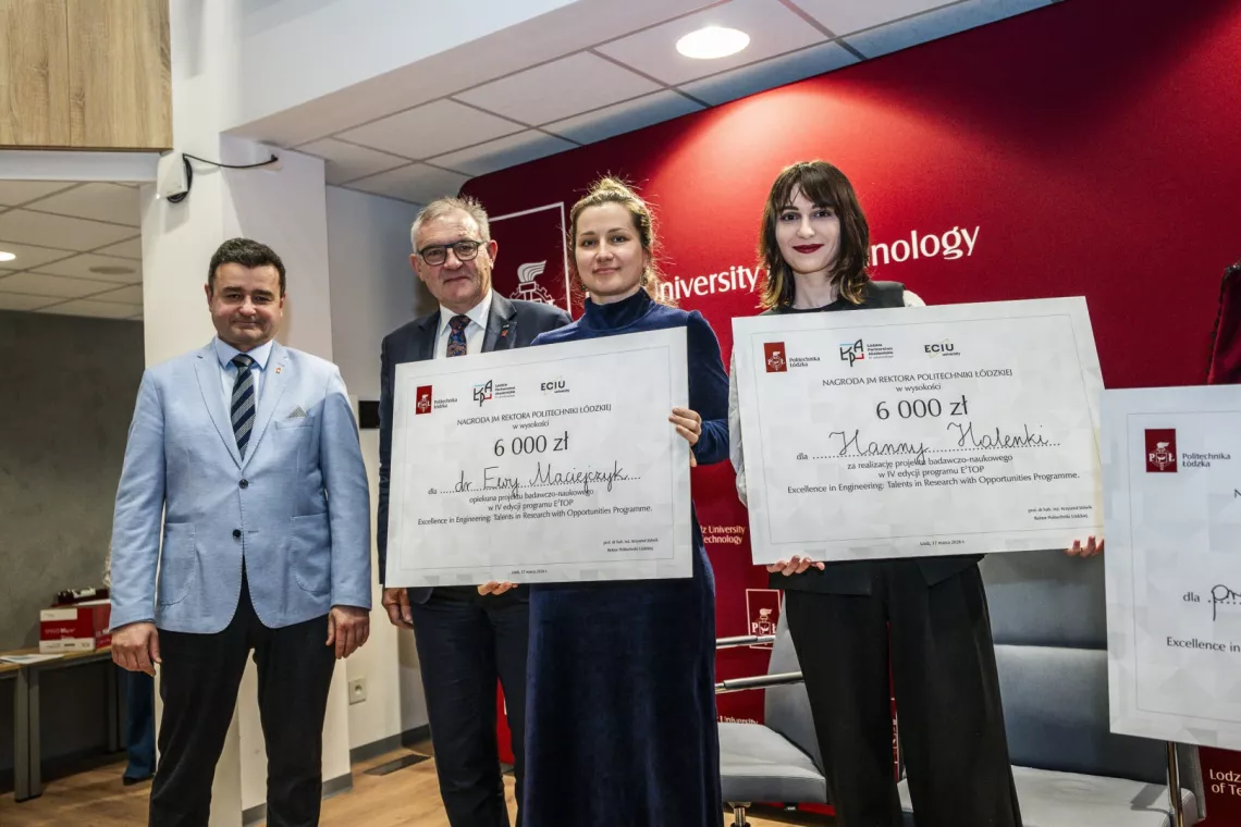 Dwie kobiety z czekiem w rekach stoją w towarzystwie dwóch elegancko ubranych mężczyzn 