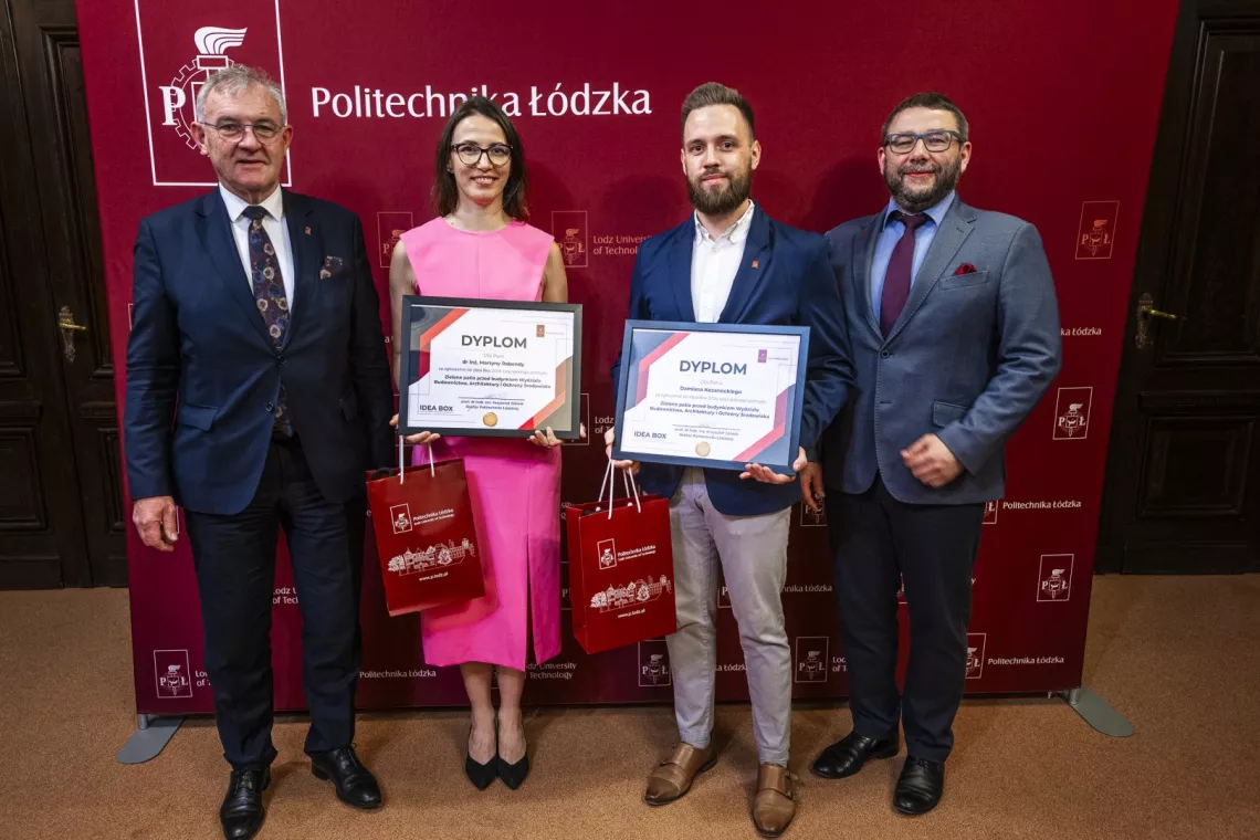 Kobieta w różowej sukience i trzech mężczyzn w garniturach na stoja na tle baneru z napisem Politechnika Łódzka . Kobieta i mężczyzna w środku trzymają w rękach dyplom.