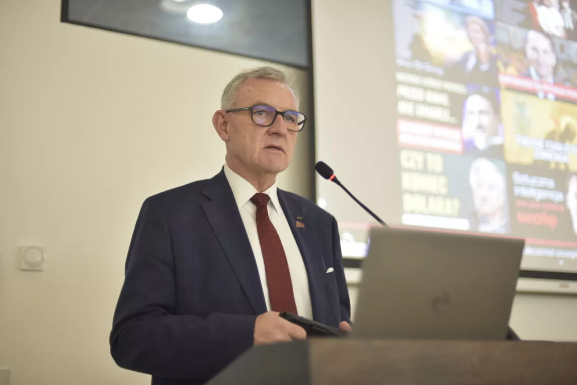 Przemawia elegancko ubrany mężczyzna 