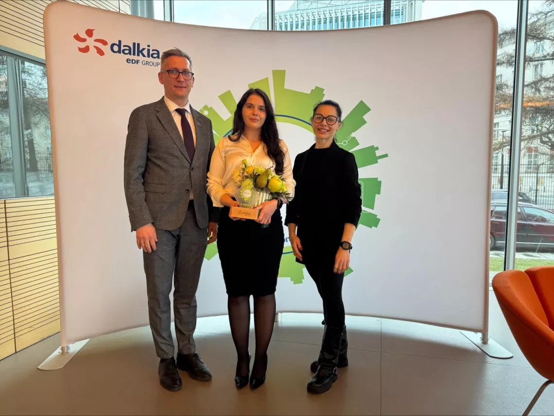 Trzy osoby stojące przed tłem z logo "Dalkia EDF GROUP". Osoba w środku trzyma bukiet kwiatów i statuetkę