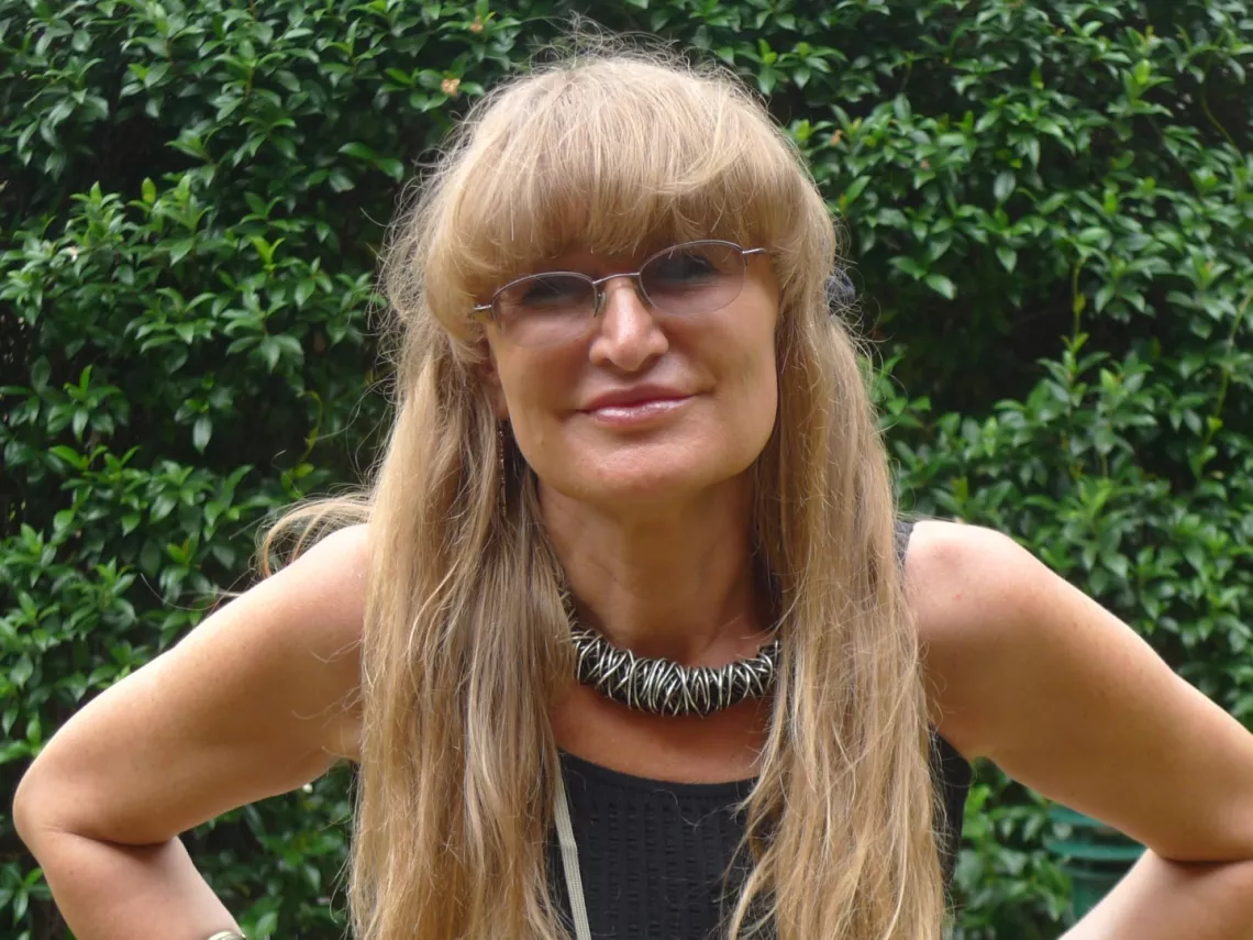 Kobieta w okularach, z długimi jasnymi włosami, sfotografowana na tle zielonej rośliny