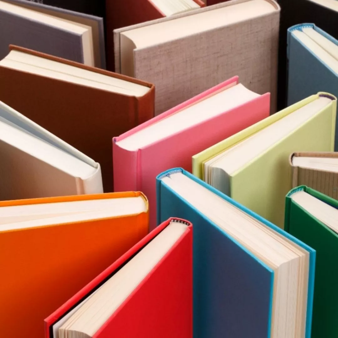 Książki w sztywnych różnokolorowych okładkach stoją ustawione w nieuporządkowany sposób.