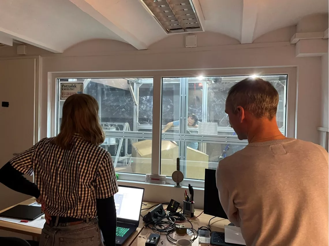 Dwie osoby widoczne od tyłu, stoją przy biurku na którym jest rozmity sprzęt