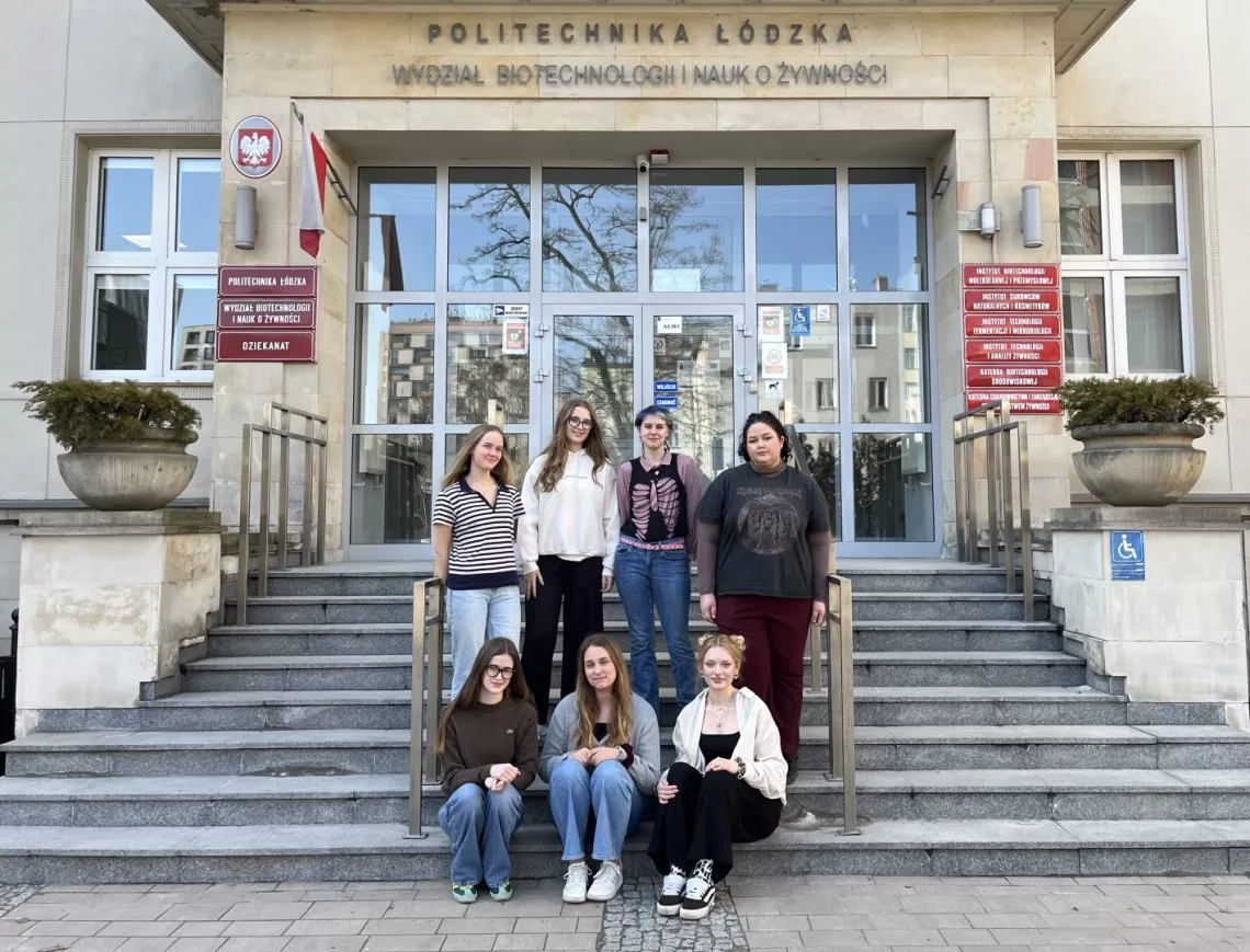 Na schodach przed budynkiem stoja cztery studentki, kolejne trzy siedzą poniżej