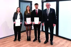 Troje studentów studentów stoi, trzymając w ręku dyplomy, towarzyszy im elegancko ubrany mężczyzna w garniturze