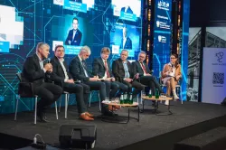 Sześć osób siedzi na podwyższeniu tworząc grupę panelową, z tyłu na ekranie wyśwetlane są zdjęcia panelistów