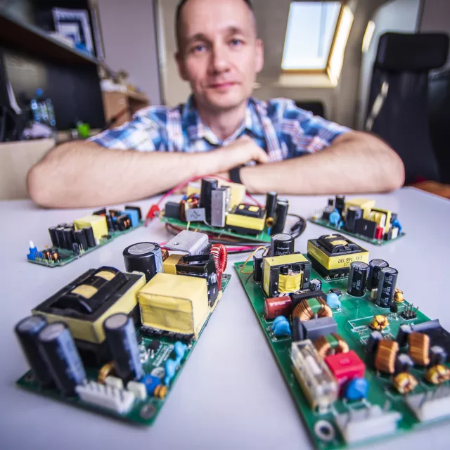 Osobę oparta o stół, na którym jest kilka płytek elektronicznych. 