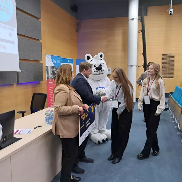 Dwie osoby odbierają nagrody, Czek trzyma kobieta, mężczyzna ściska dłoń jednej z osób.