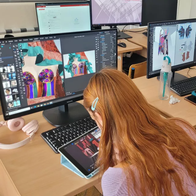 Studentki siedzą przy otwartych laptopach na których widać cyfrowe projekty modowe