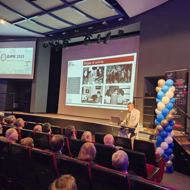 Przemawia mężczyzna, stojąc za mównicą. Na ekranie wyświetla się slajd 