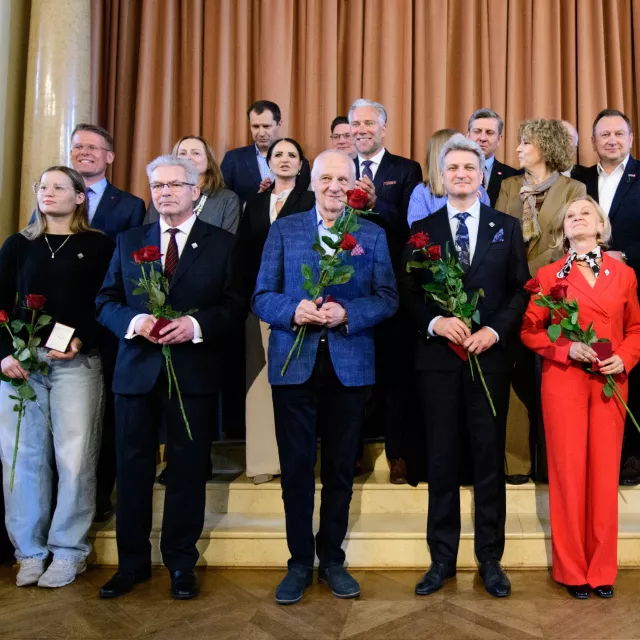 Grupowe zdjęcie, osoby stojące w pierwszym rzędzie osoby trzymają róże w ręku 