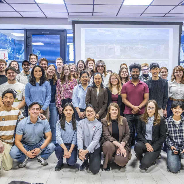 Liczna grupa młodych osób na zbiorowym zdjęciu w sali seminaryjnej, w tle okno i ekran projekcyjny